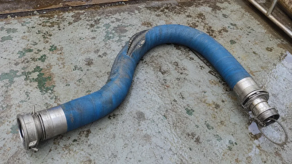 Mangueira industrial azul com terminais metálicos e dano localizado após transporte offshore