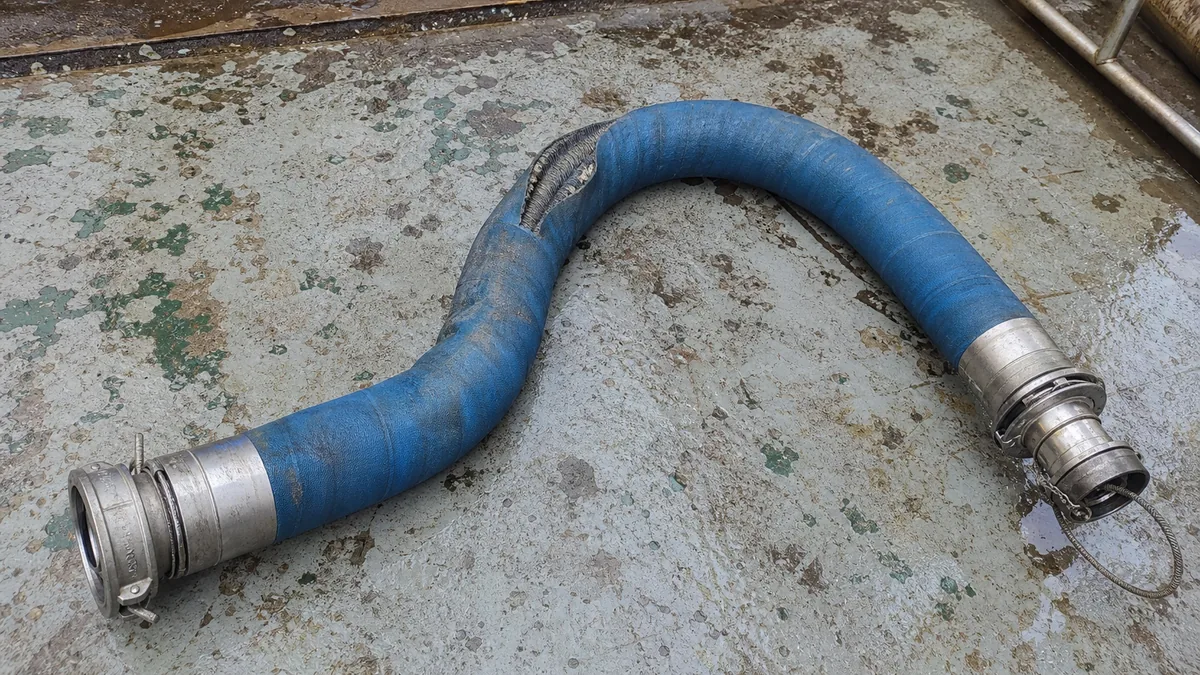 Mangueira industrial azul com terminais metálicos e dano localizado após transporte offshore